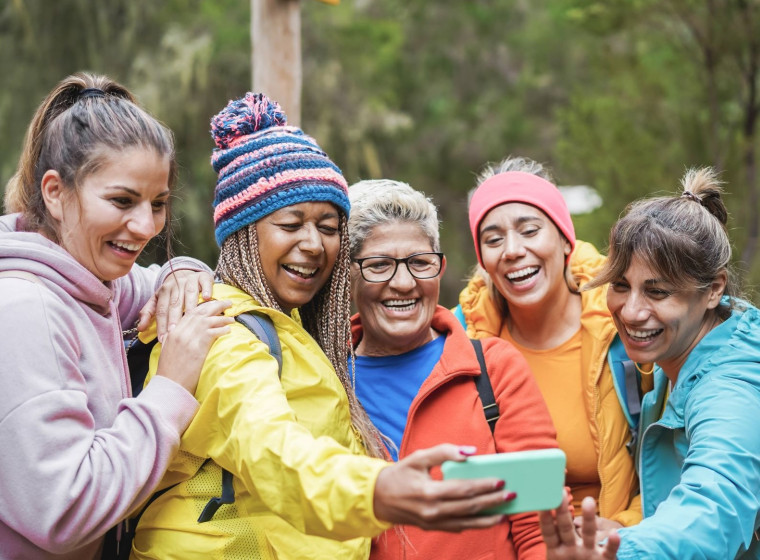 Five smiling women of various ages in colourful jackets take a selfie together.