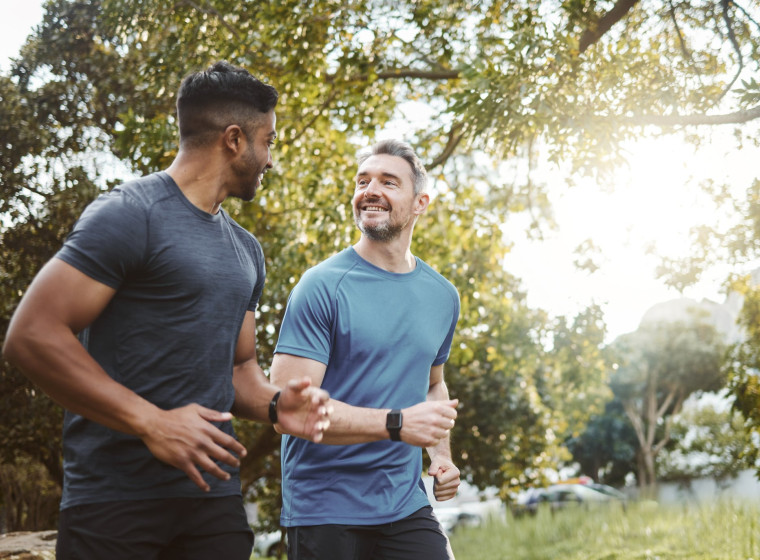 A photo of two young men chatting while jogging in a park. 